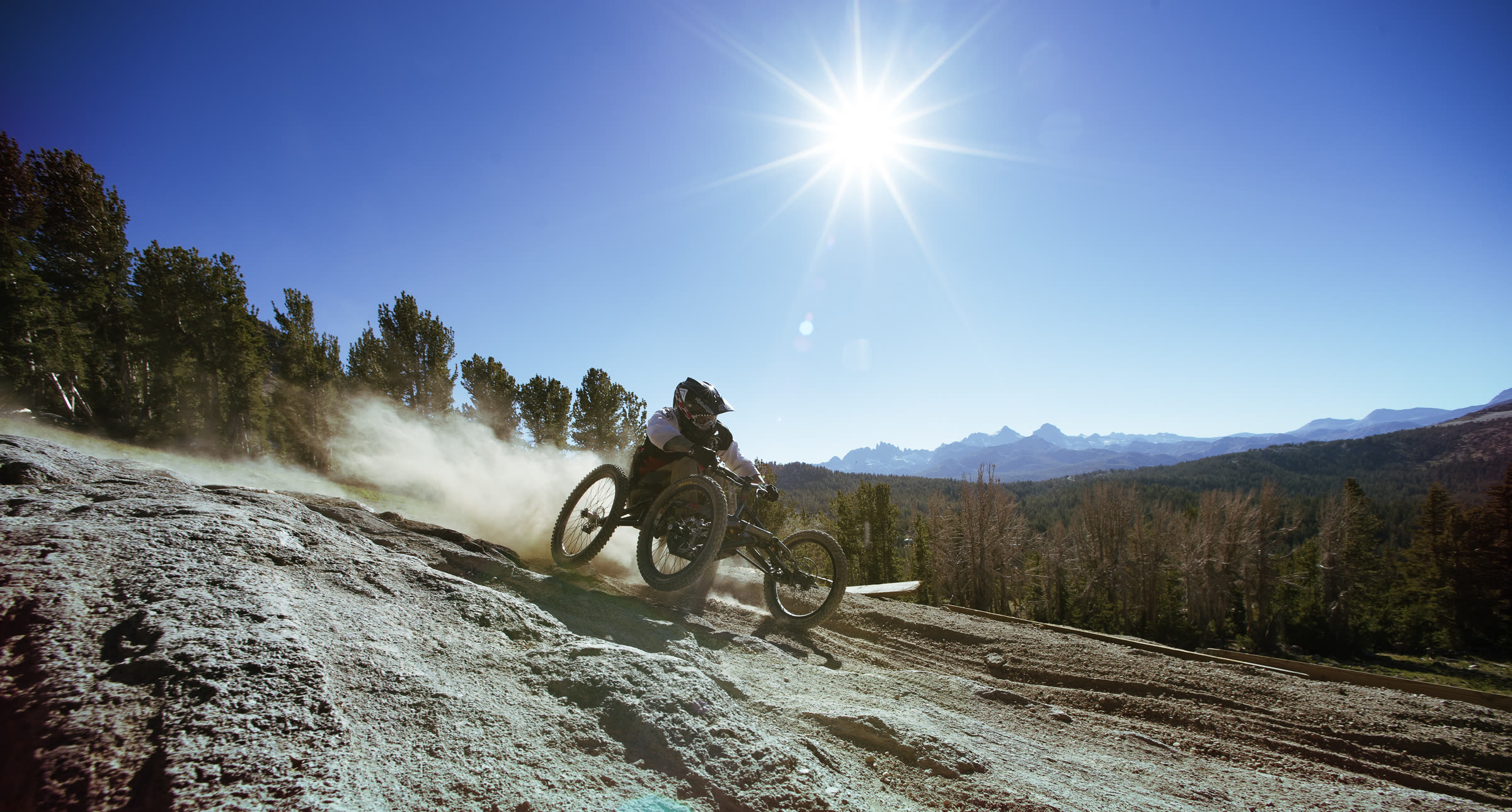 Adaptive mountain bike rider descending a rocky ridge with the sun behind